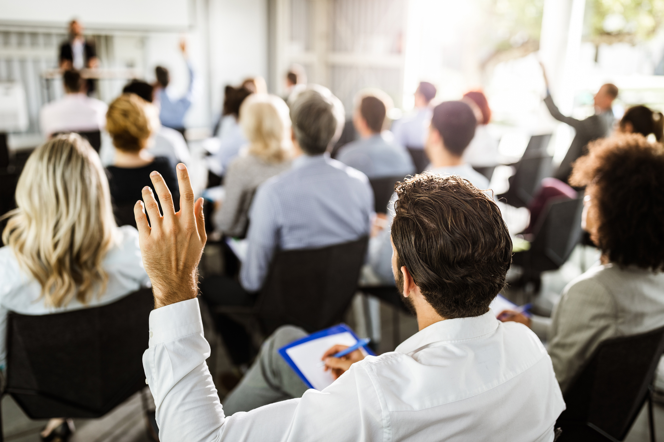 Rear view of a businessman raising his hand to ask the question on a seminar with large group of his colleagues.