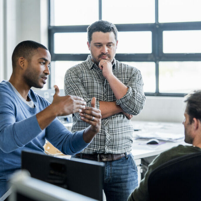 A photo of businessman sharing ideas with colleagues at workplace. Confident male professional is discussing with coworkers. They are wearing smart casuals in creative office.